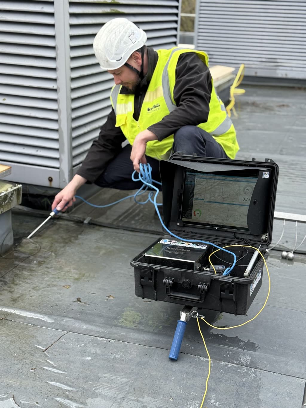 A Trace Surveys surveyor using a probe on a flat roof beside an instrument case.