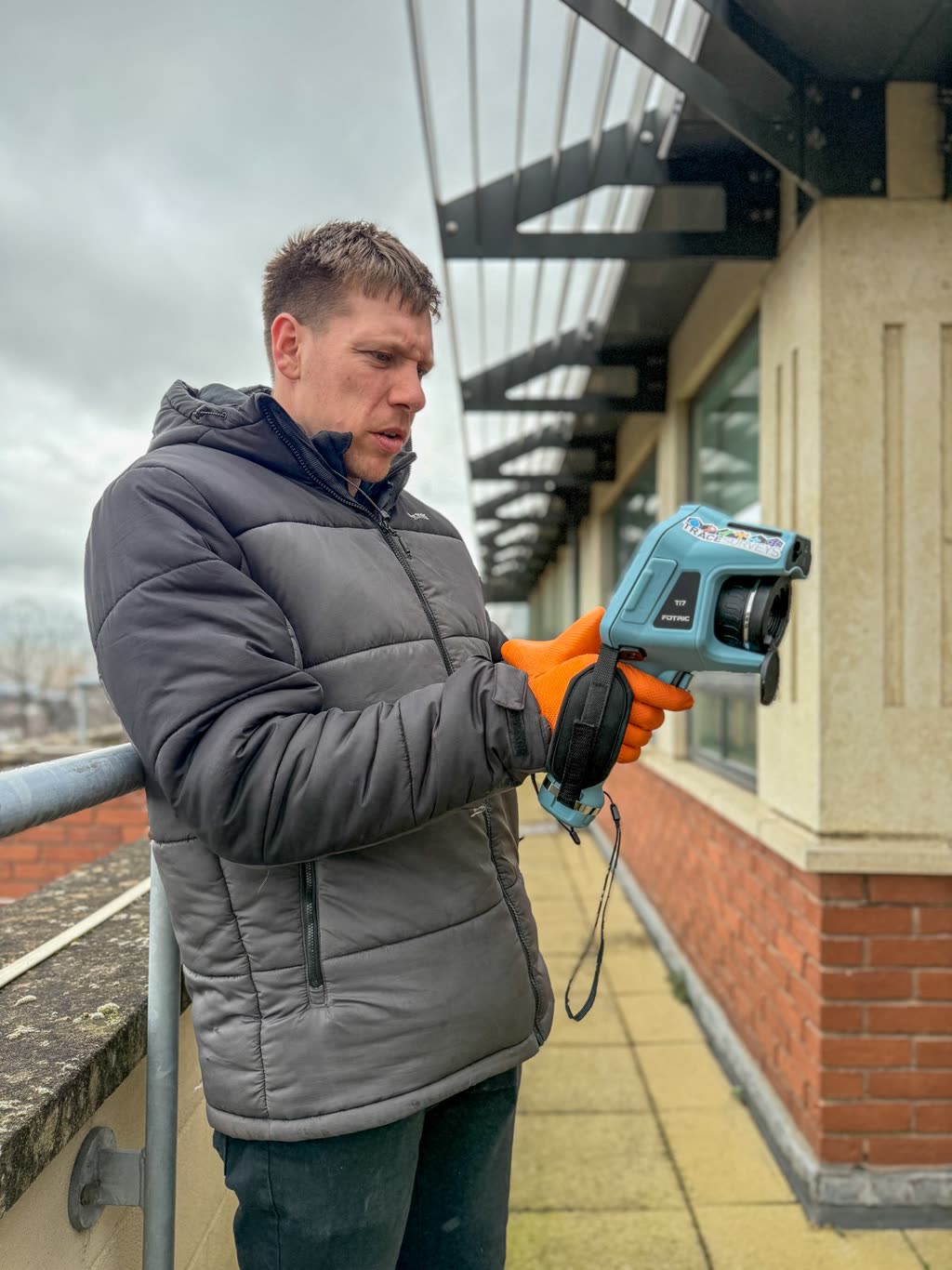 A Trace Surveys surveyor using a handheld thermal camera on a building elevation.